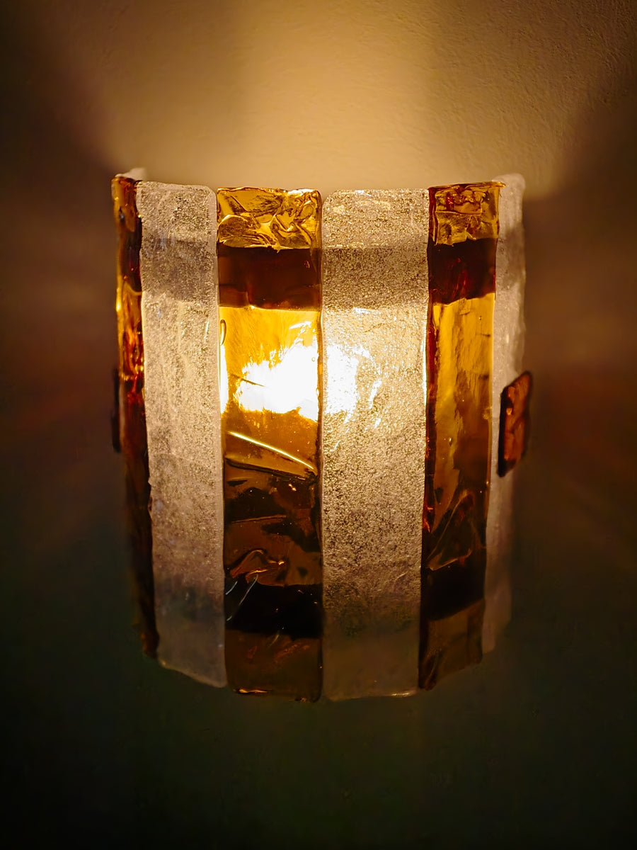 Wall-mounted sconce with striped amber and clear glass panels lit from within with beams radiating outwards