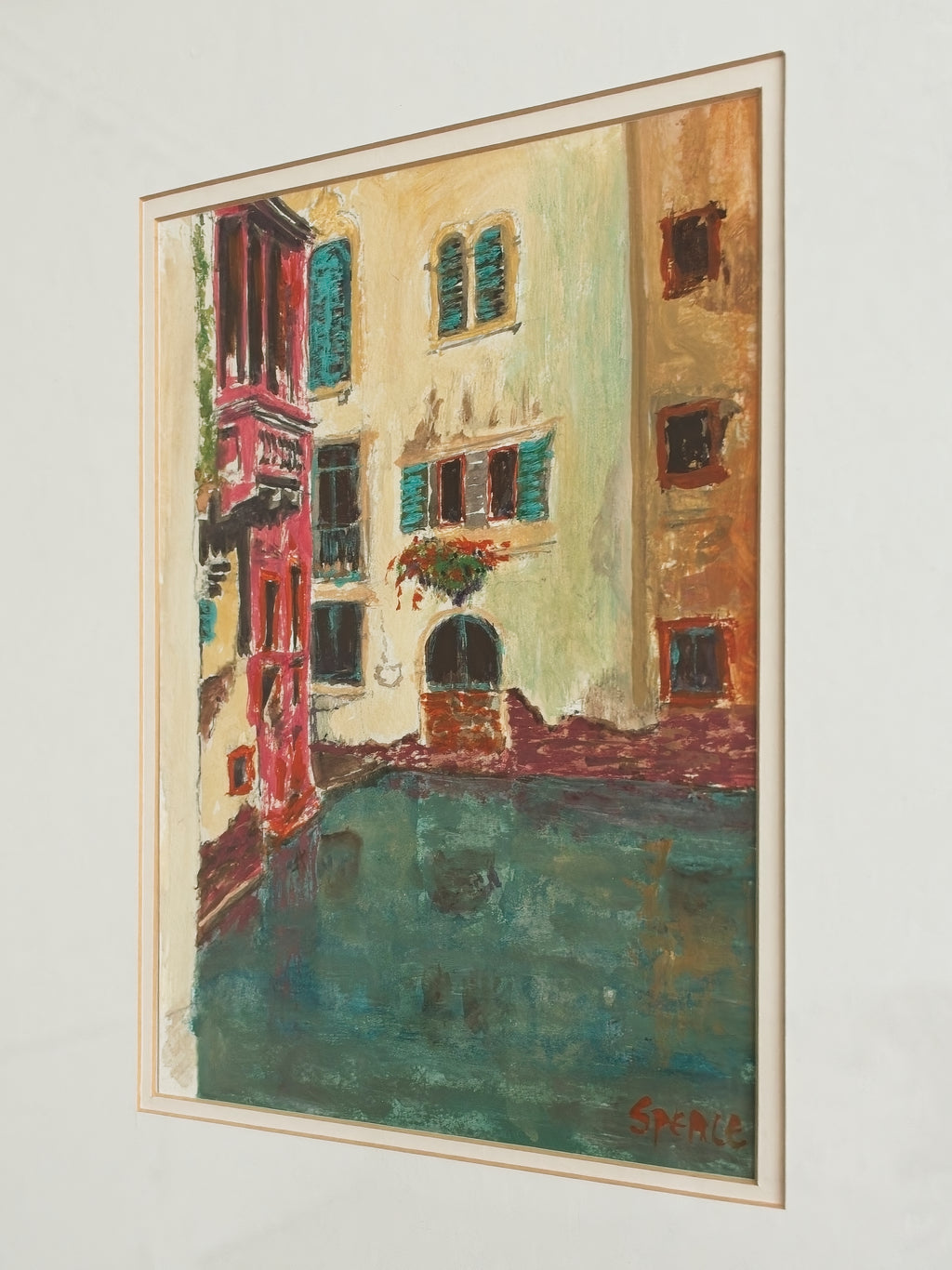 A close up of an original framed vintage watercolour artwork of a brightly coloured Venice canal scene on a white wall.