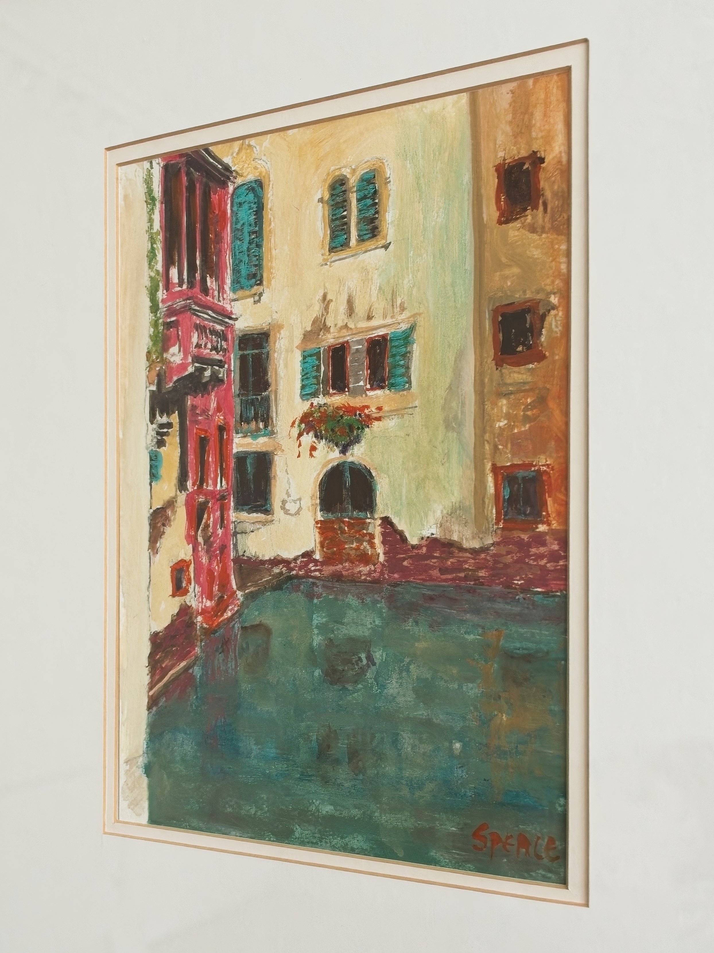 A close up of an original framed vintage watercolour artwork of a brightly coloured Venice canal scene on a white wall.