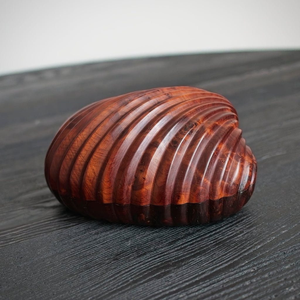 A vintage mid century modern solid walnut seashell-shaped trinket box on a dark surface.