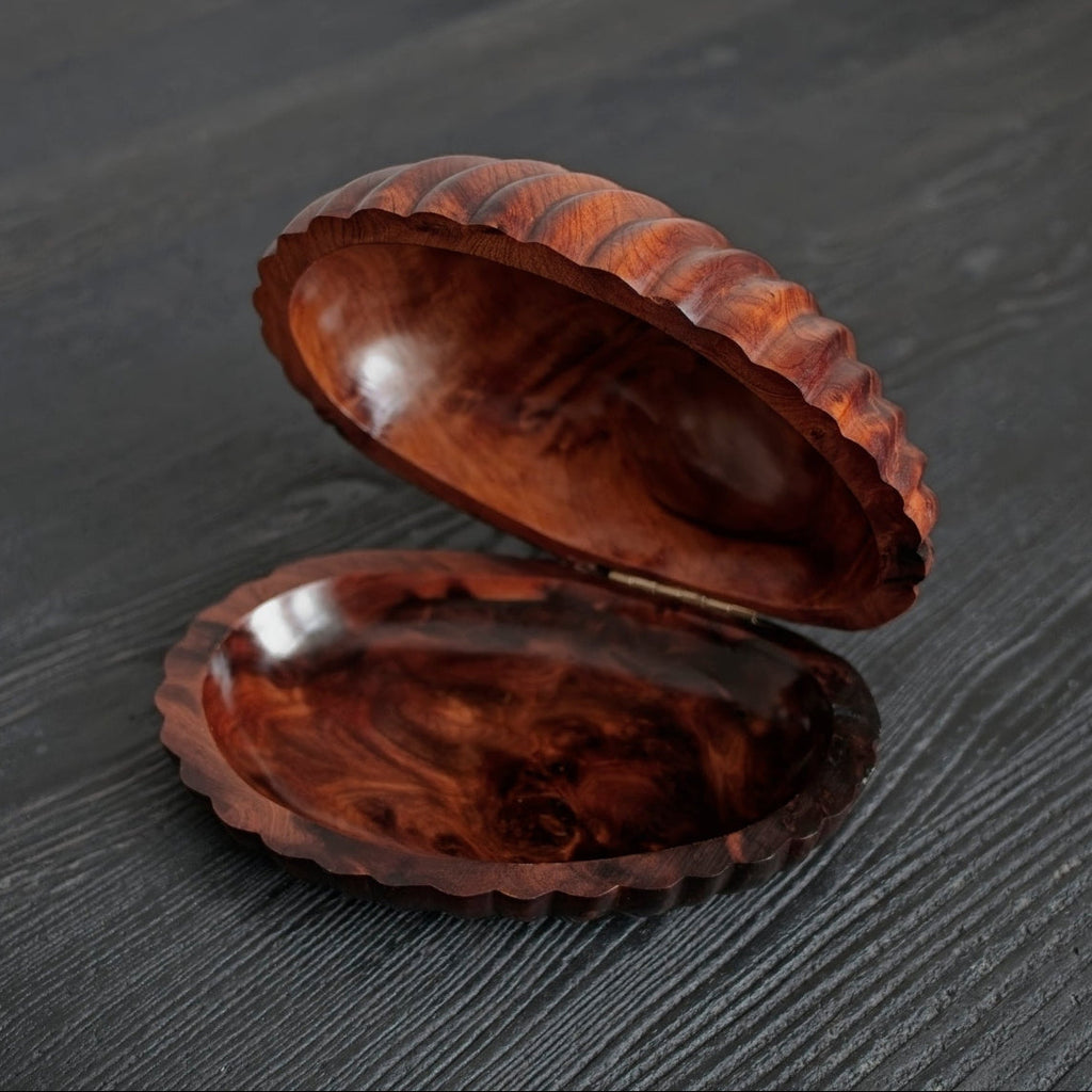 An open vintage 1960s walnut shell shaped trinket box from above on a textured dark surface.