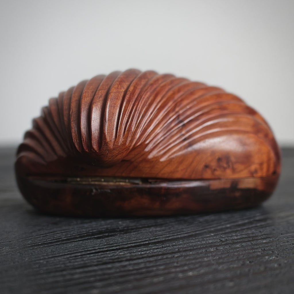 A close up of the back of a vintage piece of home décor for sale. A mid century modern wooden shell-shaped trinket box on a dark surface with a light grey background.