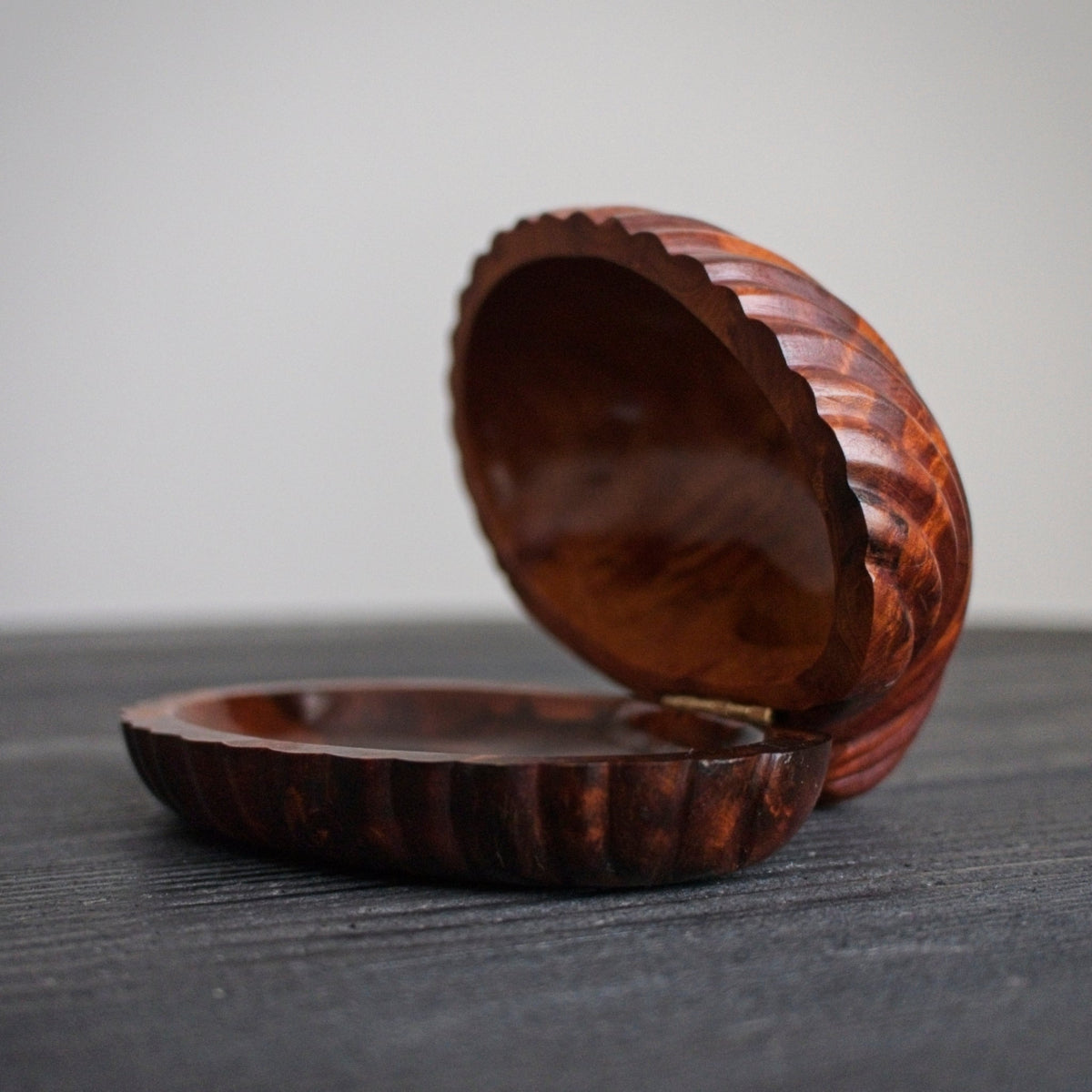 A small mid century modern vintage walnut clamshell shaped trinket box with the lid open on a dark surface.