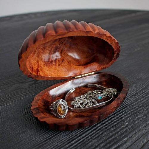 Vintage mid century modern walnut clamshell-shaped trinket box containing silver jewellery on a dark surface.