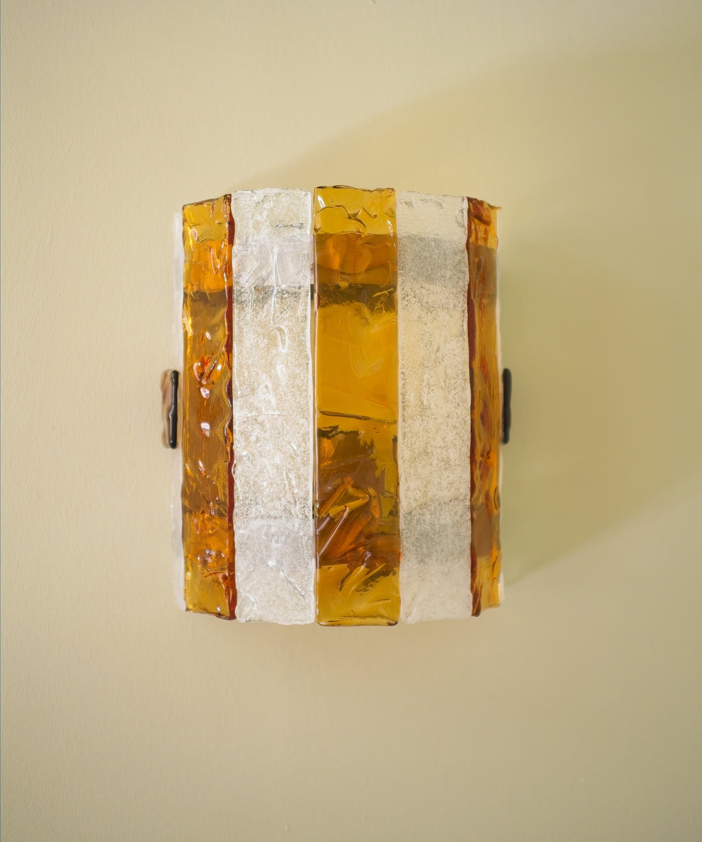 Decorative wall sconce with amber and white striped glass panes on a light green wall.