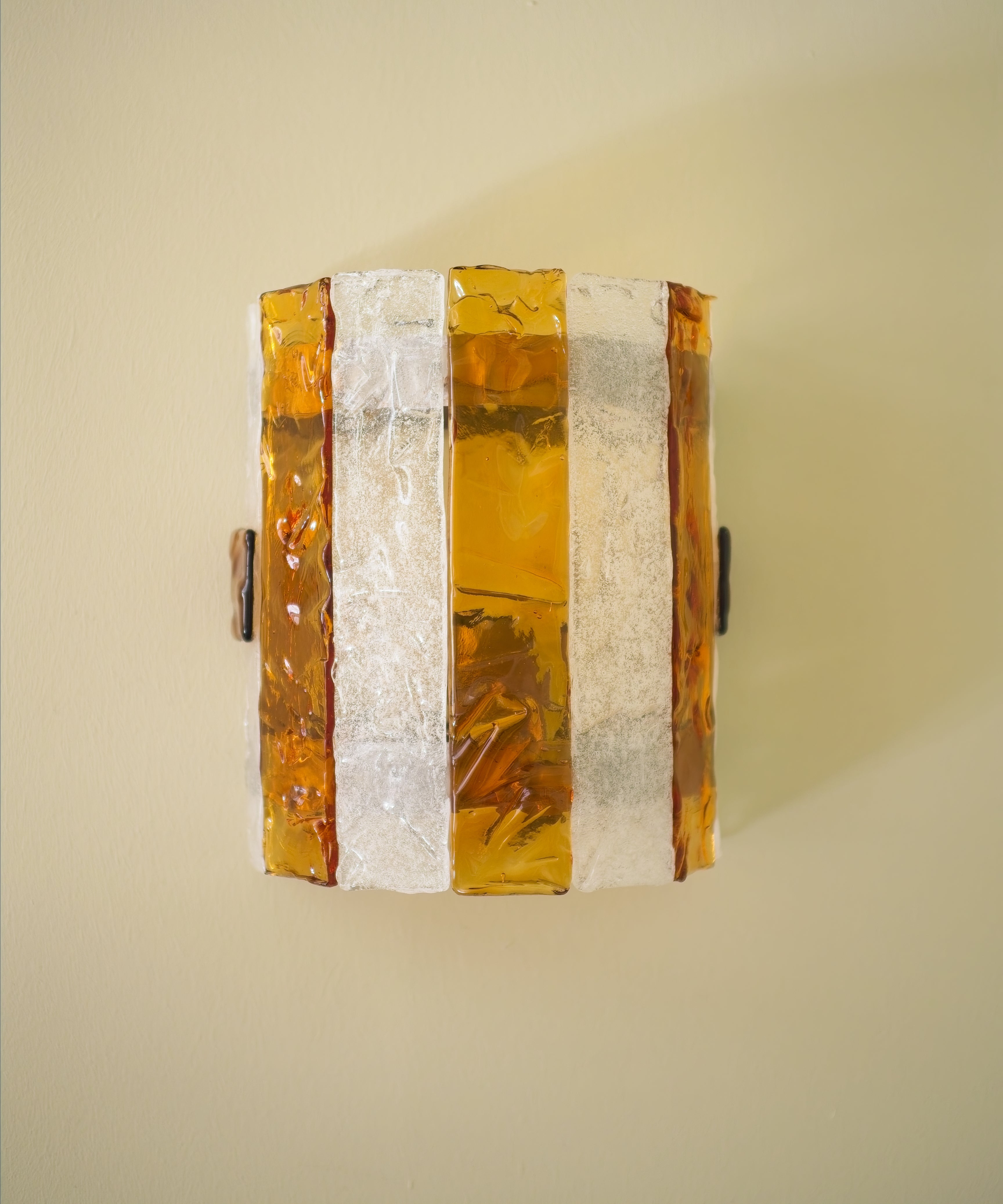 Decorative wall sconce with amber and white striped glass panes on a light green wall.