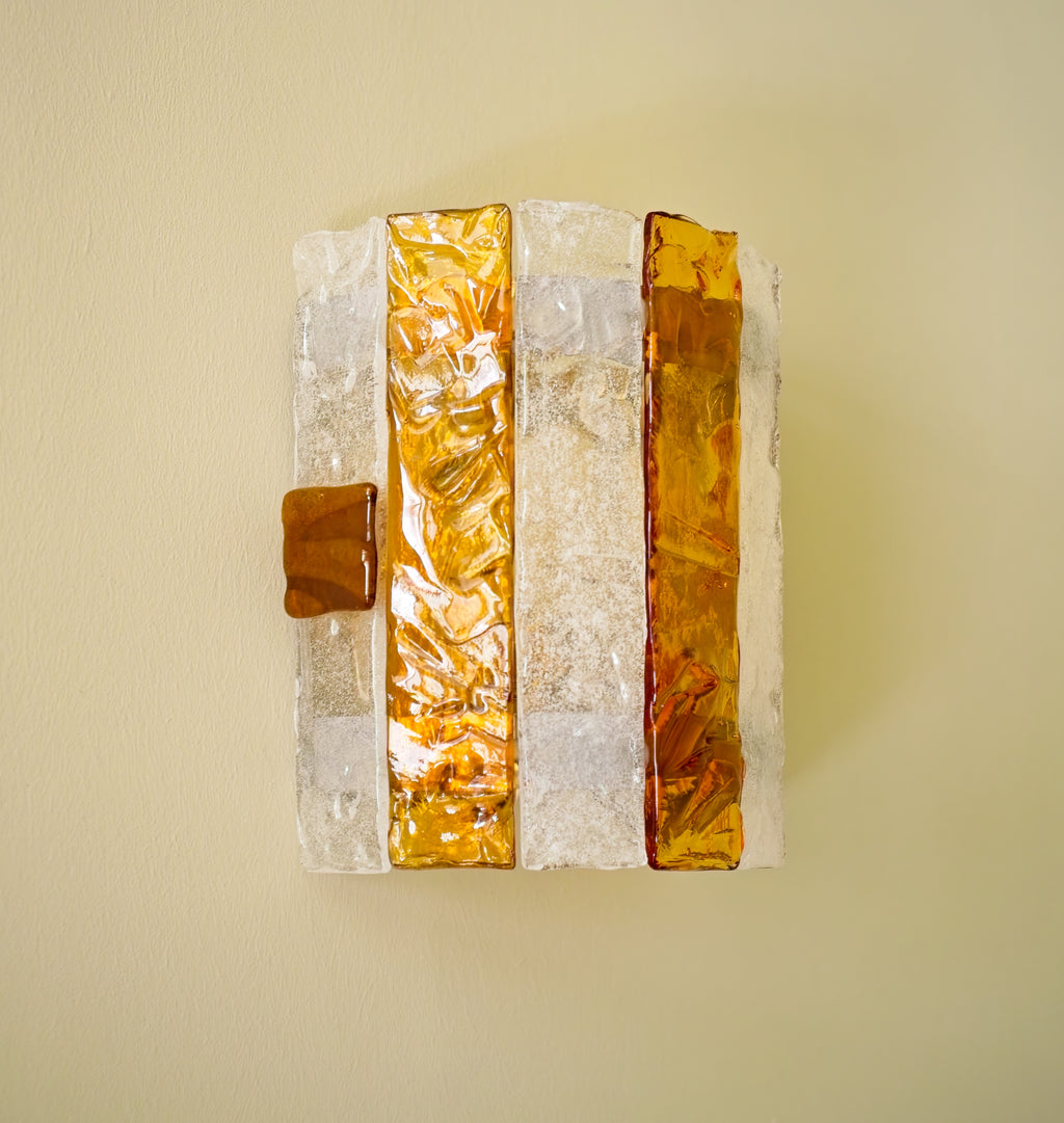 Decorative wall sconce with amber and white striped panels on a light green background.