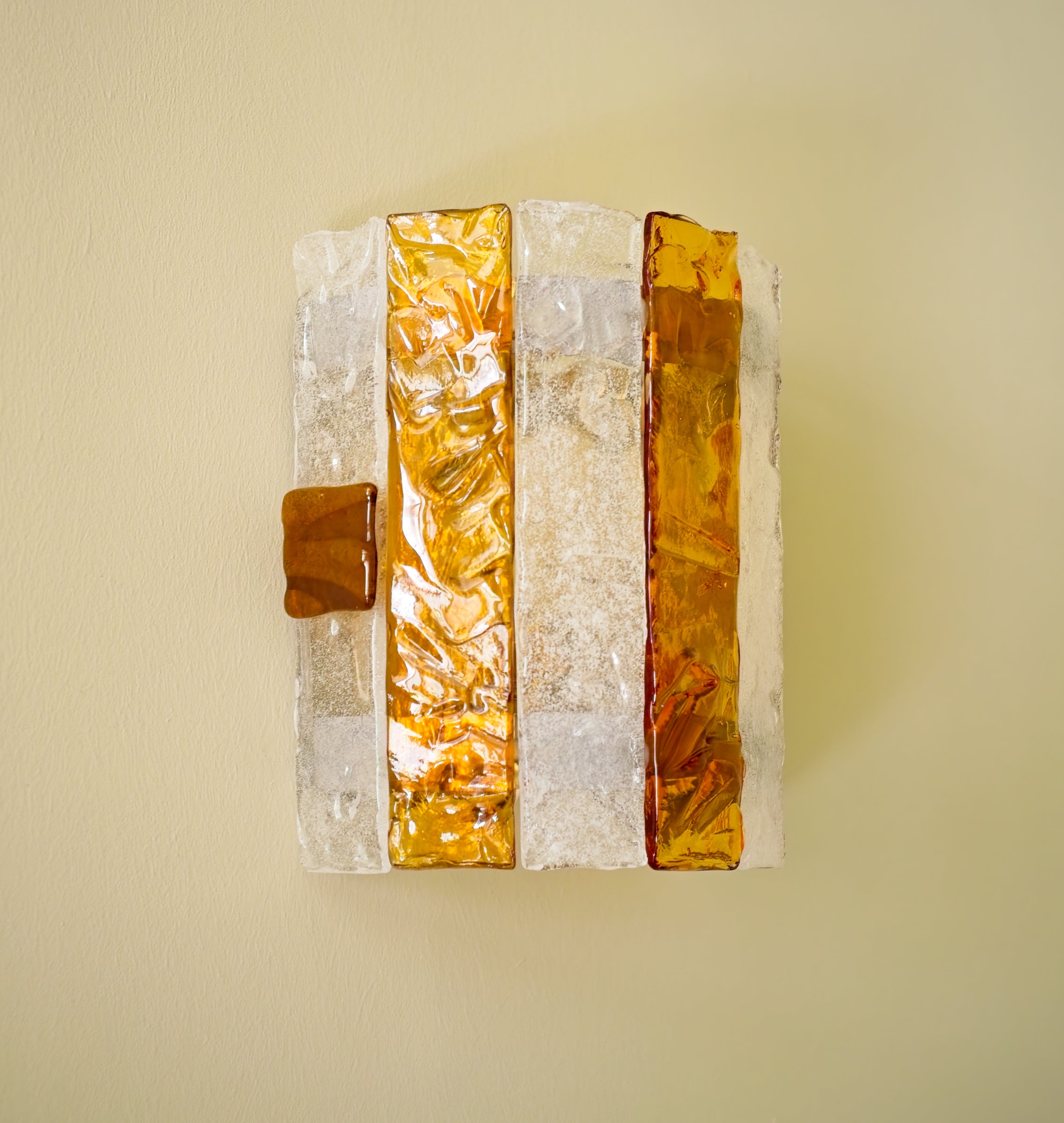 Decorative wall sconce with amber and white striped panels on a light green background.