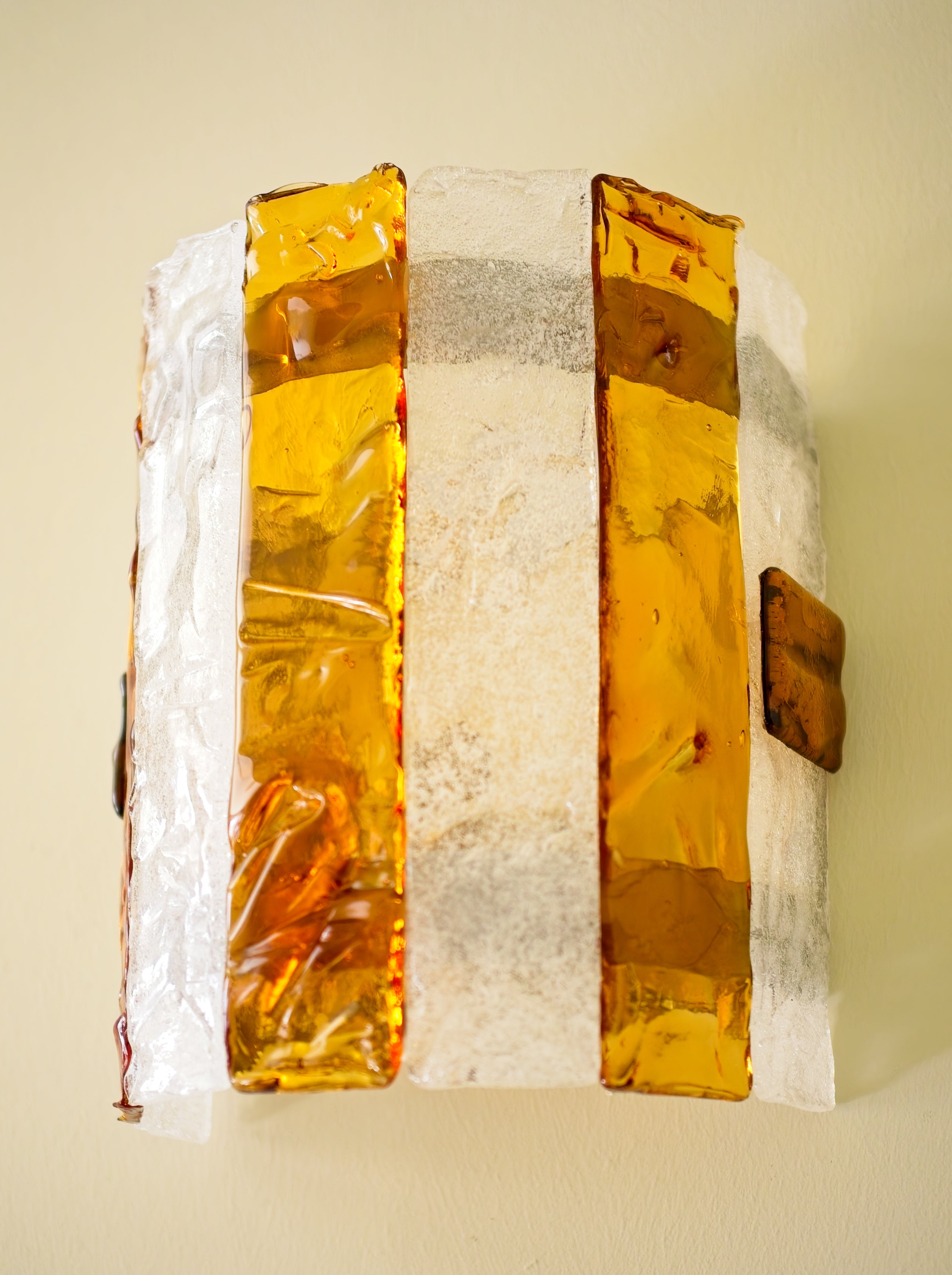 Close up of a decorative wall sconce with amber and clear glass panels on a light green wall.