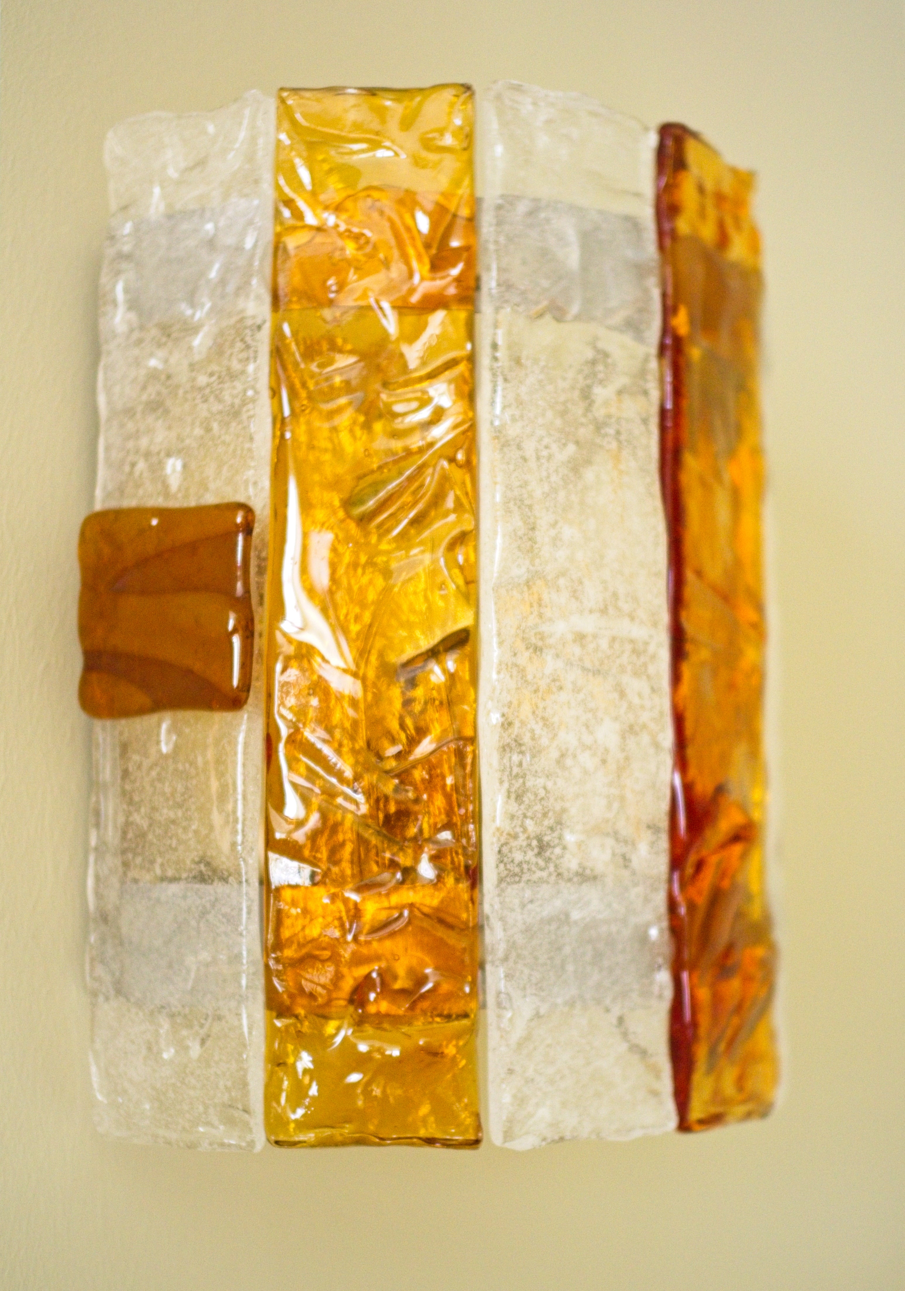 Close up profile of a rectangular wall sconce with amber and clear glass elements on a light green background.