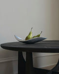 Two pears in an vintage mid century modern angular silver dish on a black wooden table in front of a plain background.
