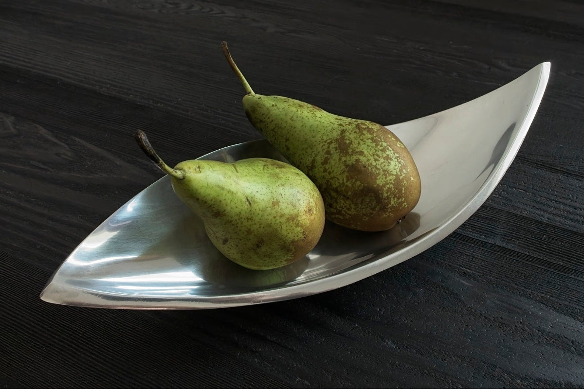 Two pears on a silver leaf-shaped dish against a dark background