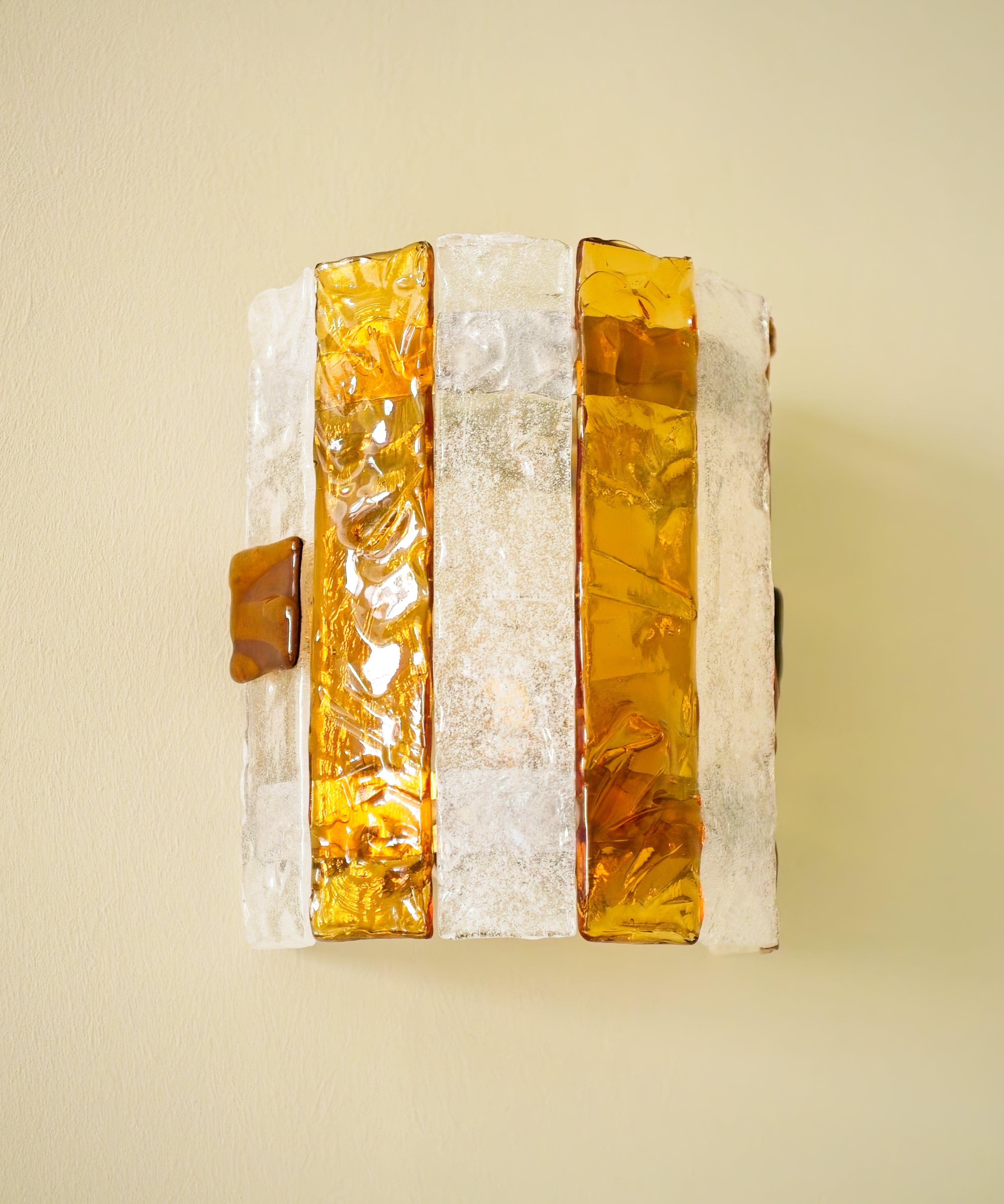 Decorative wall sconce with amber and white striped glass panes on a light green background.