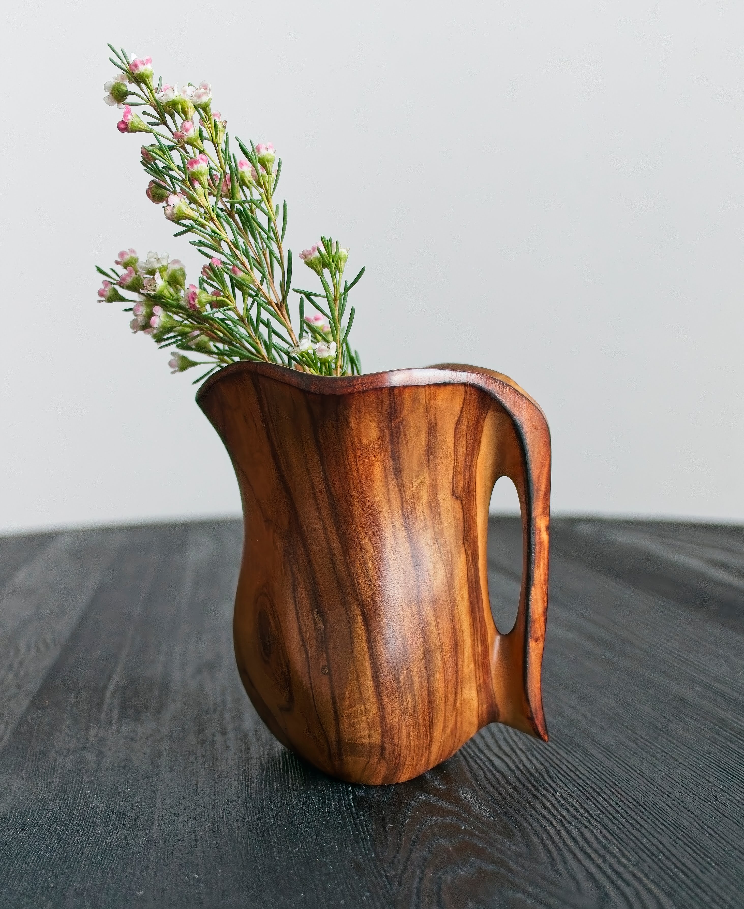 A small vintage decorative wooden vase containing rustic pink flowers on a dark surface with a light grey background.