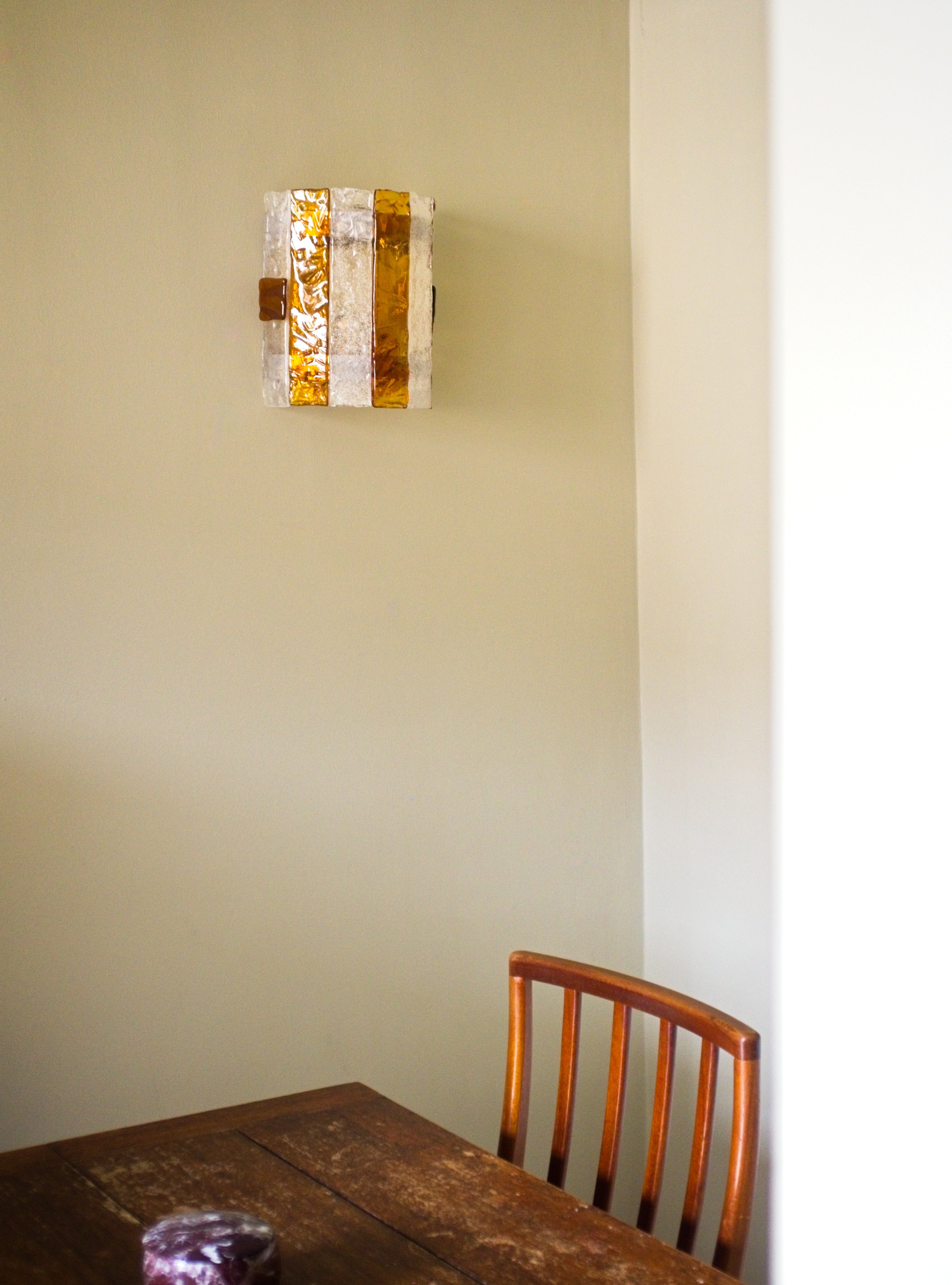 Wall-mounted light fixture on a light green wall with a wooden chair and table in the foreground.