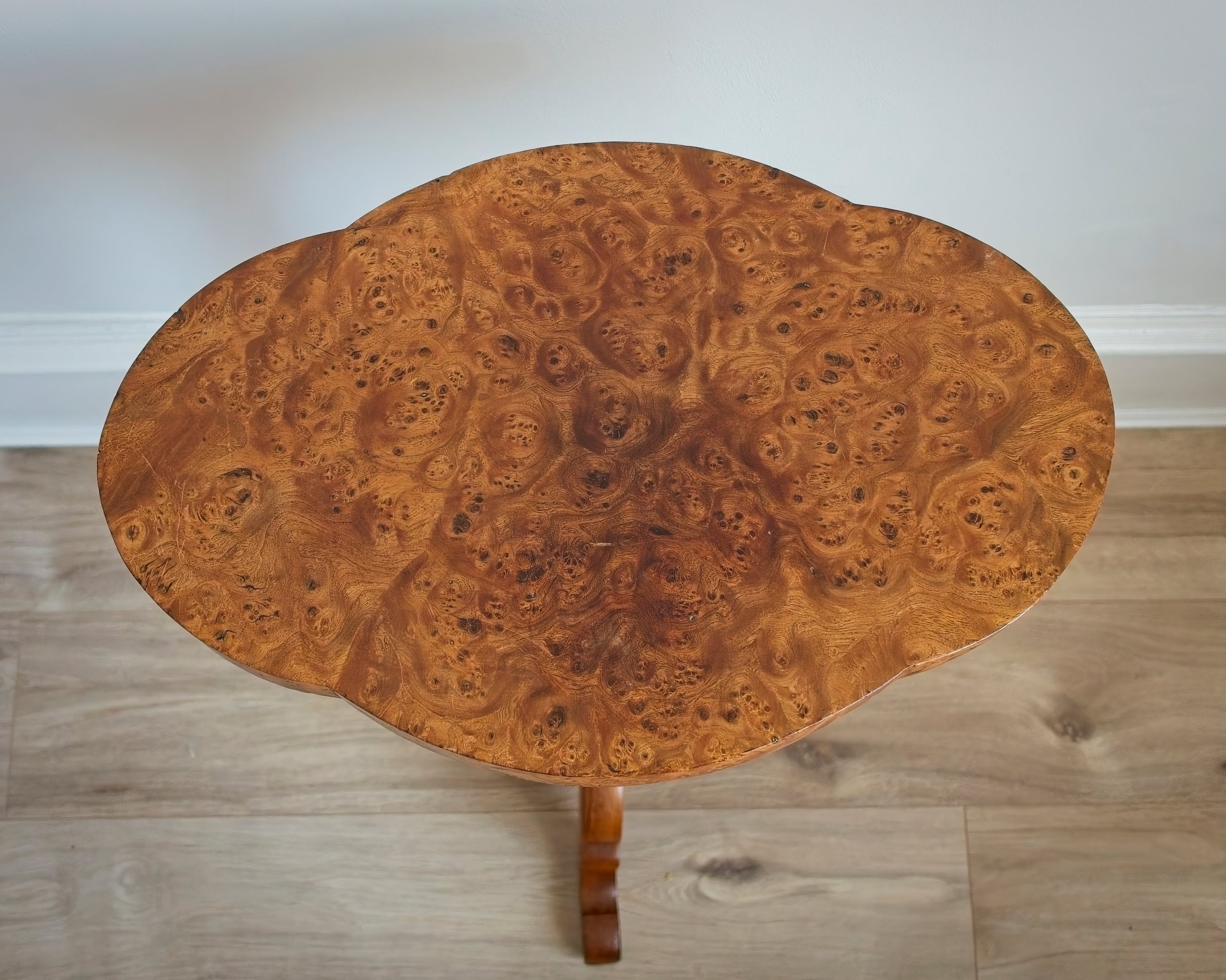 A birds eye view of the flower shaped top of a knotted maple burr wood side table on a wooden floor.