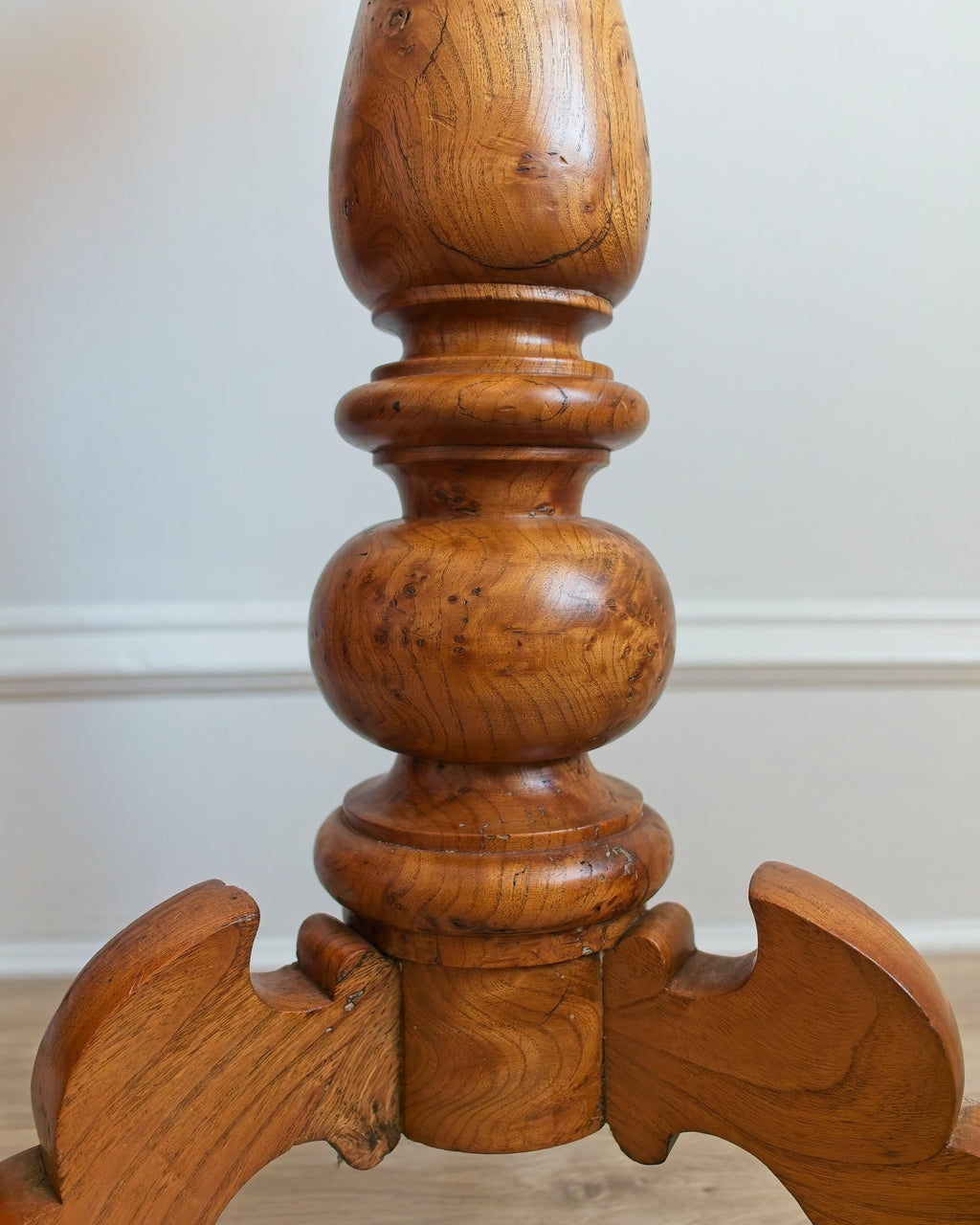 A close-up of the spindle of a Georgian style maple burr wood side table with intricate carvings against a neutral background.