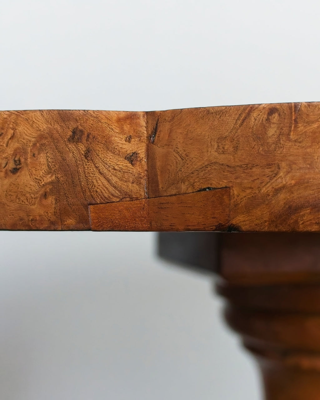 Close-up of a vintage maple burr wood table top with a plain background.