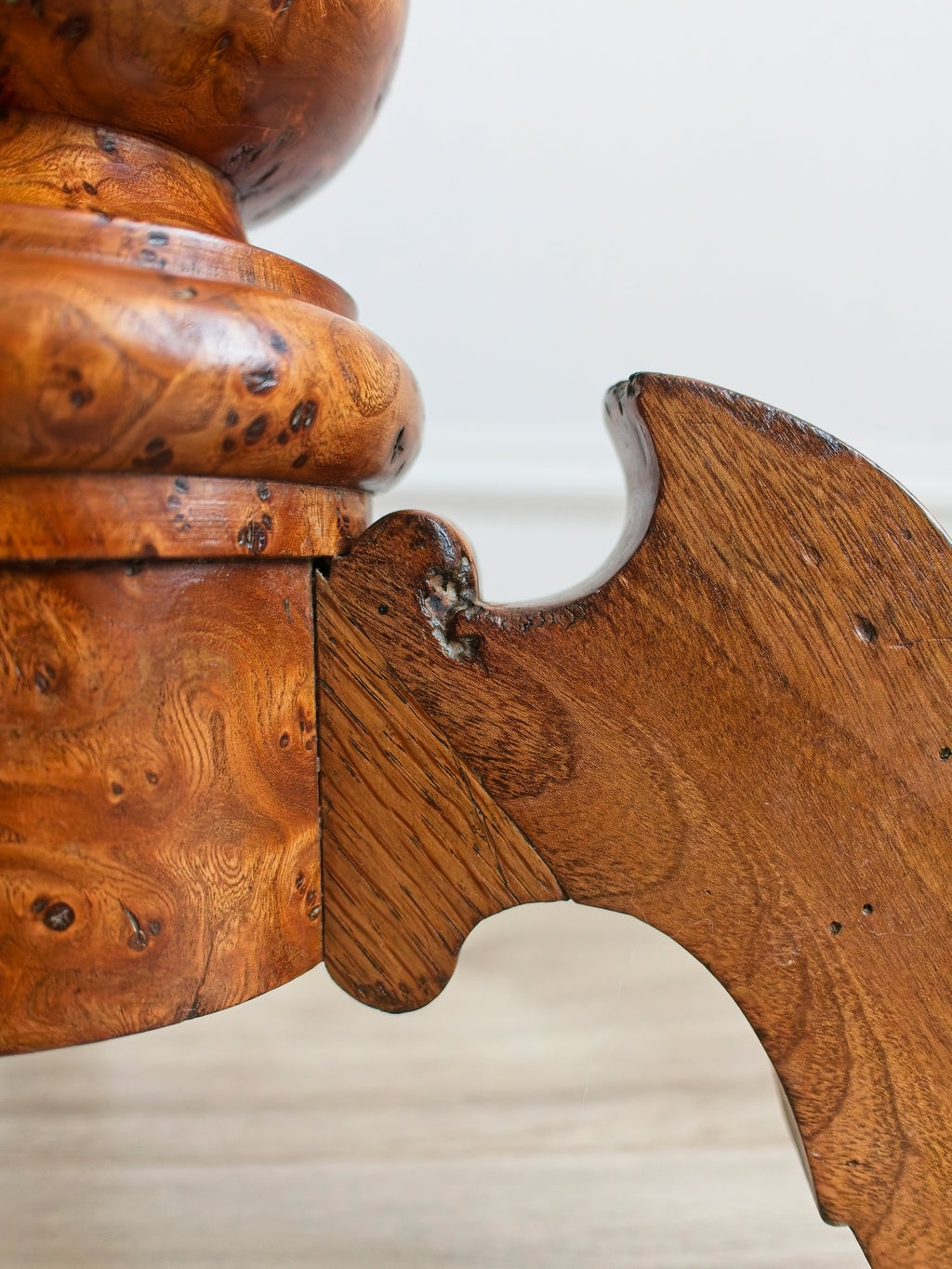 Close-up of the carved leg of a vintage maple burr wood accent table with intricate carvings on a white background.