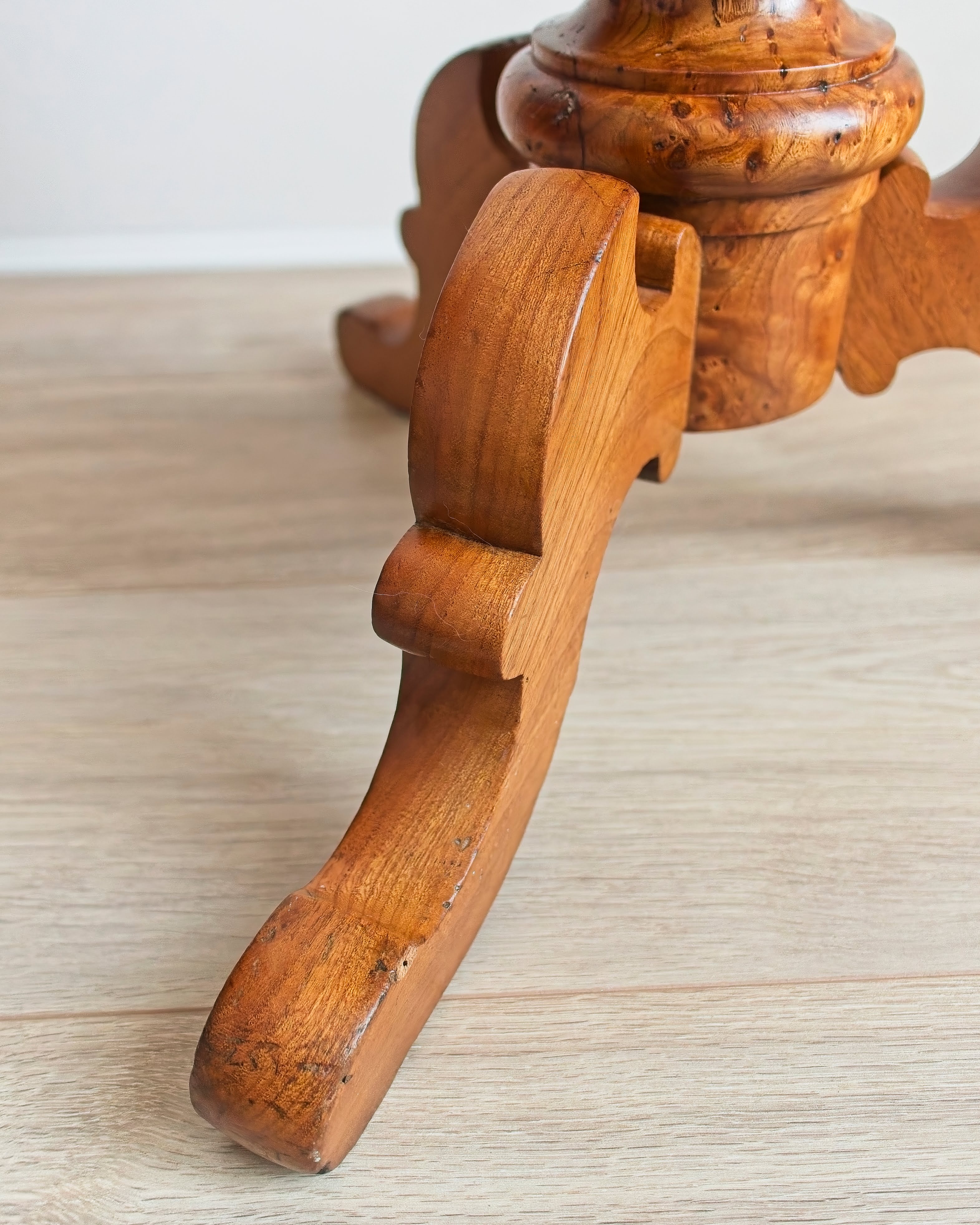 Close-up of an antique maple burr wood table leg on a light wooden floor.