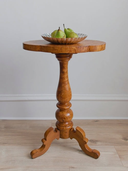 An antique Georgian maple burr wood side table with a silver scallop edged bowl containing pears on a plain background.