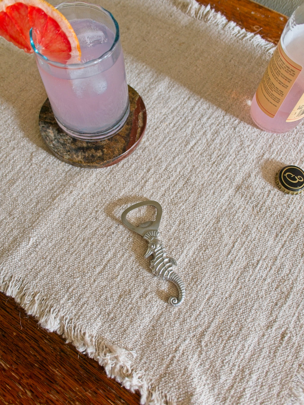 Vintage mid century modern art deco pewter seahorse bottle opener by Just Andersen on a textured surface with a pink cocktail in the background.