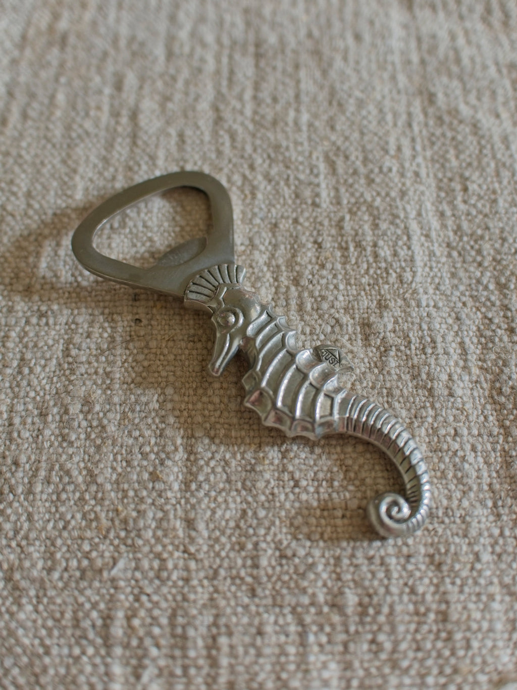 A close up of a vintage 1930s pewter seahorse bottle opener by Danish designer Just Andersen featuring the makers engraving of 'Just' in a triangle on the seahorses fin.