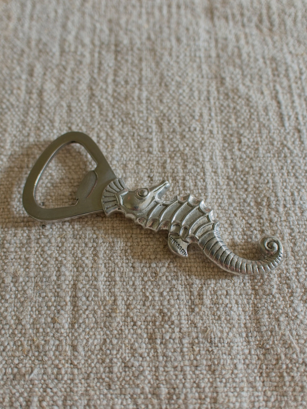 A close up of a vintage 1930s pewter seahorse bottle opener by Danish designer Just Andersen featuring the makers engraving of 'Denmark' on the seahorses fin.