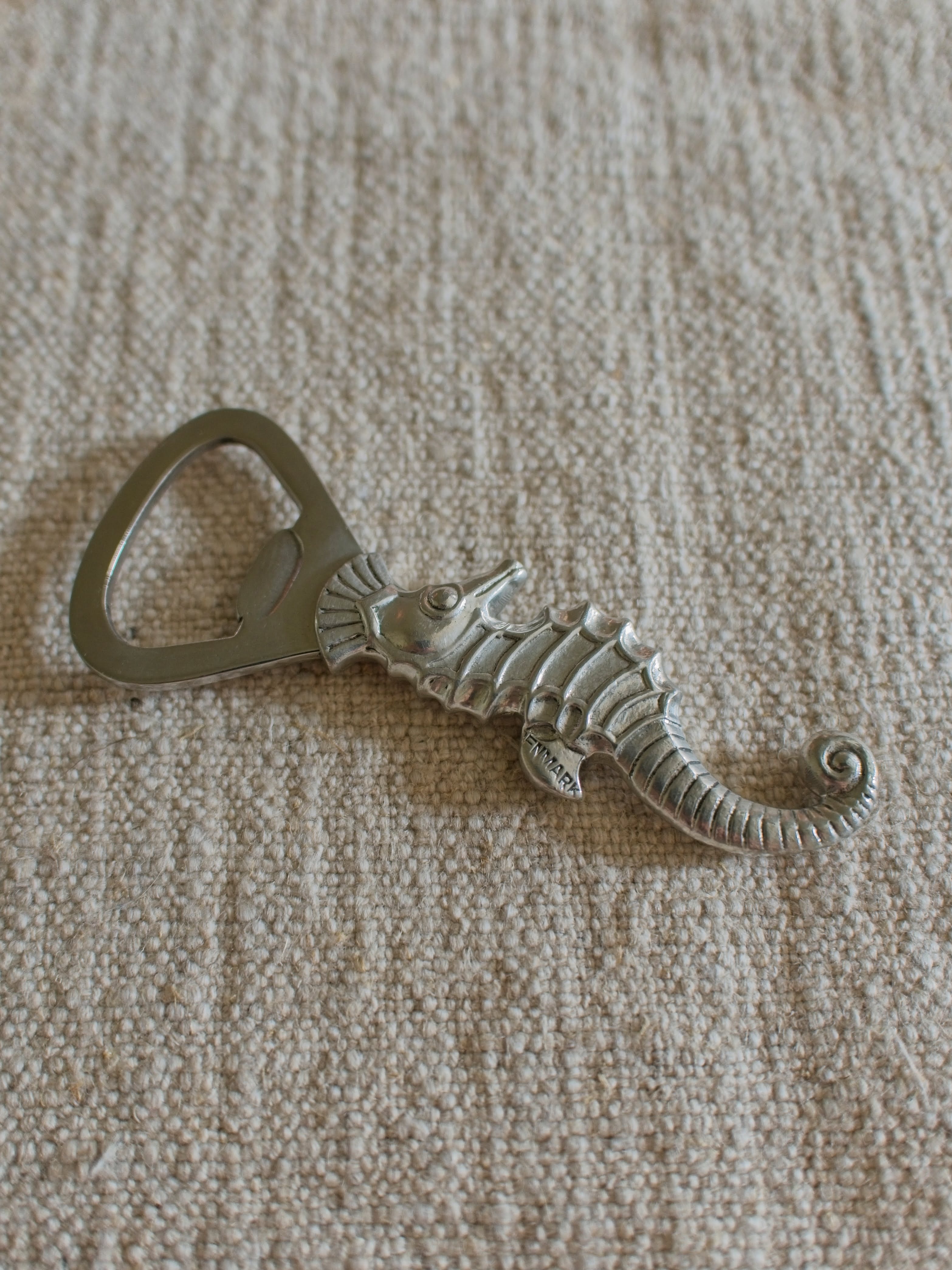 A close up of a vintage 1930s pewter seahorse bottle opener by Danish designer Just Andersen featuring the makers engraving of 'Denmark' on the seahorses fin.