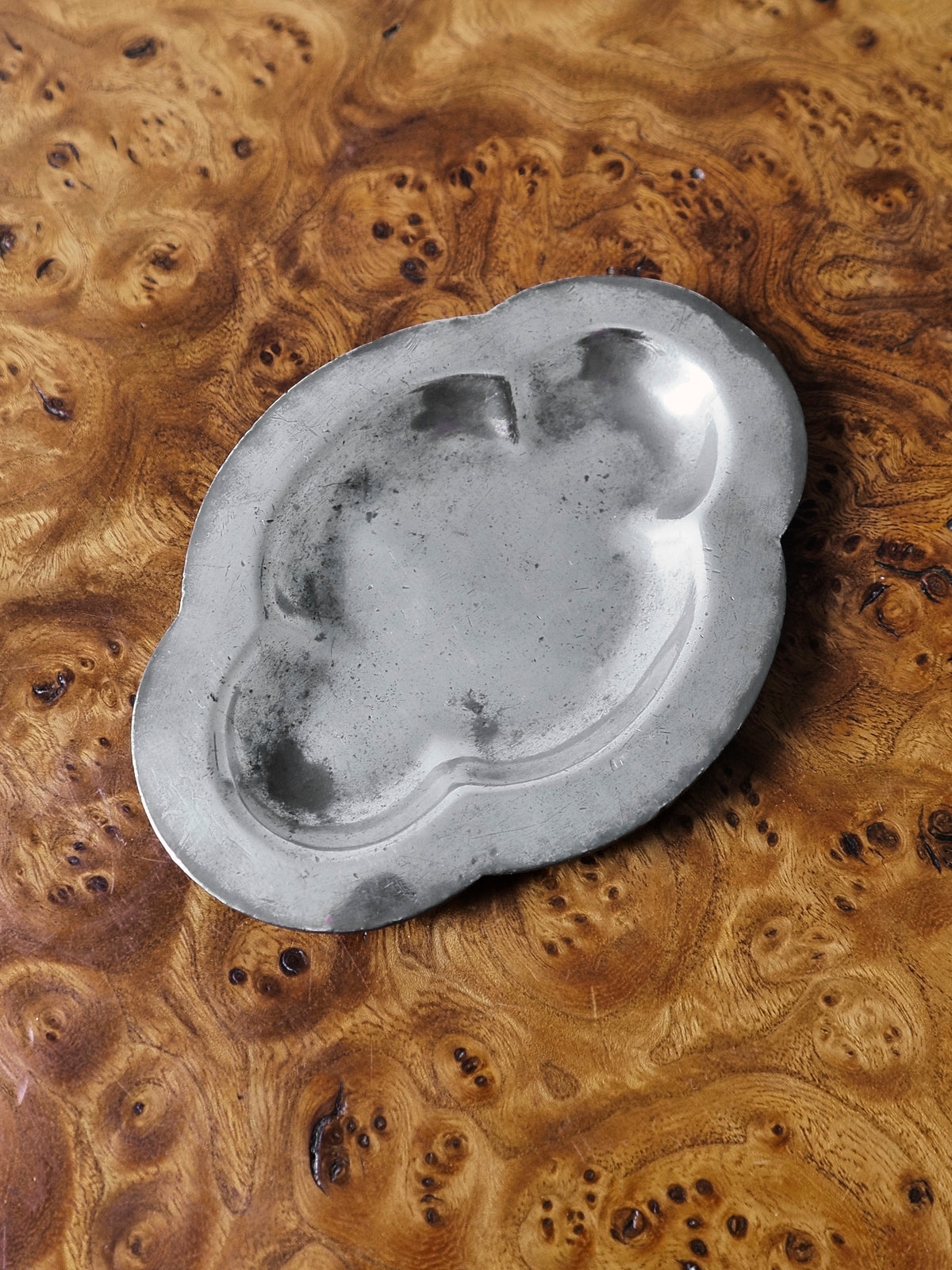 A small vintage art deco pewter ring dish by Just Andersen for GAB Sweden on an antique burl wood side table. The bijou floral shaped 1920s silver modernist trinket dish has four rounded petals and would make an cool and interesting addition to mid century modern, retro, baroque, modern vintage and minimalist home interiors.