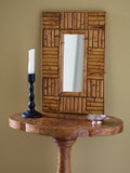 A vintage 1970s wall mounted bamboo mirror by UK modern vintage home décor store Vintrovia resting on an antique burl wood side table with a vintage bobbin wood candle holder and a silver modernist ring dish in front of a yellow wall. This mid century modern mirror is hand crafted using individual honey-toned rattan pieces to form a geometric check design that creates an interesting, modernist aesthetic. A versatile retro wall décor piece that would elevate boho, eclectic, coastal and rustic home interiors.