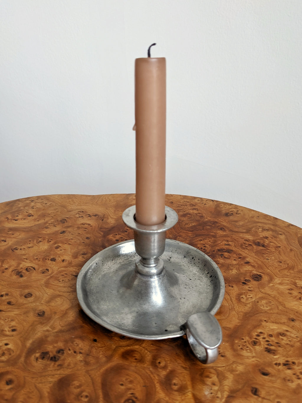 A pink candle in a vintage pewter circular candlestick holder on a wooden surface with a white background from the back.