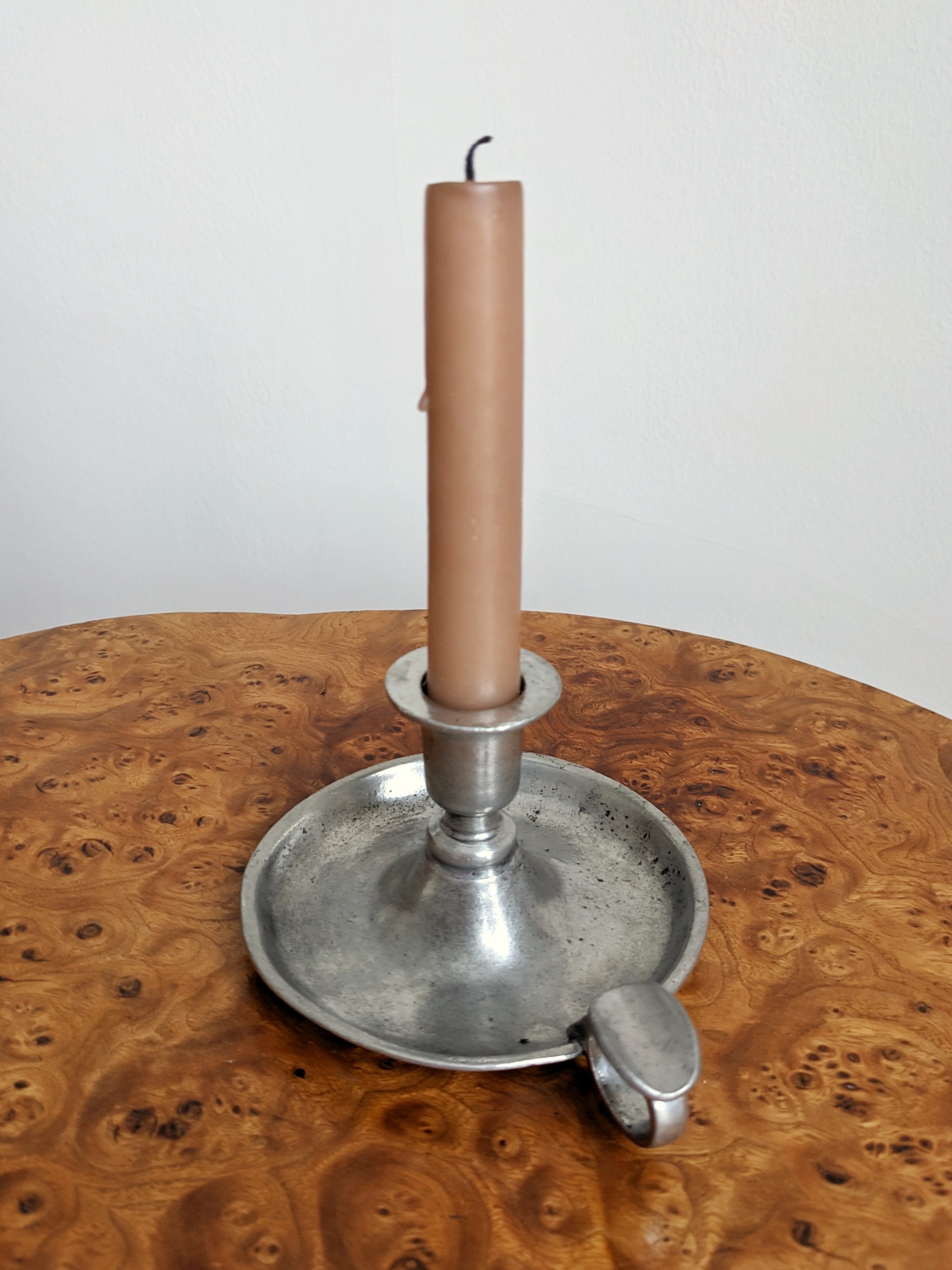 A pink candle in a vintage pewter circular candlestick holder on a wooden surface with a white background from the back.