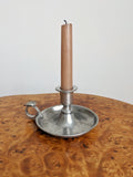 A pink candle in a vintage pewter candle holder on a burr wooden surface with a white background.