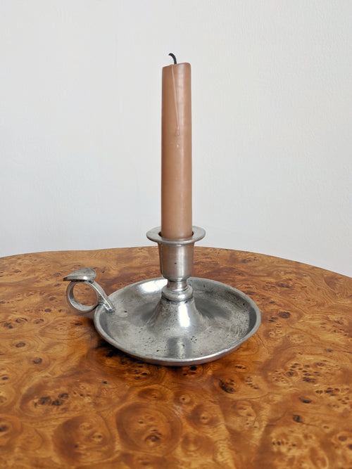 A pink candle in a vintage pewter candle holder on a burr wooden surface with a white background.