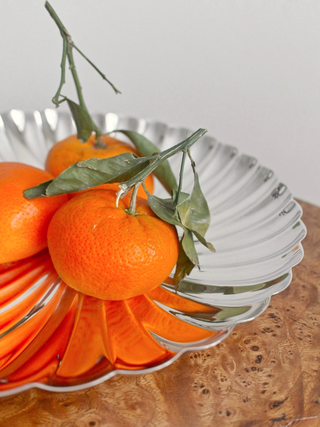 A close up of the right hand side of a vintage scallop edged fruit bowl containing three orange on top of a Georgian antique burr wood side table.