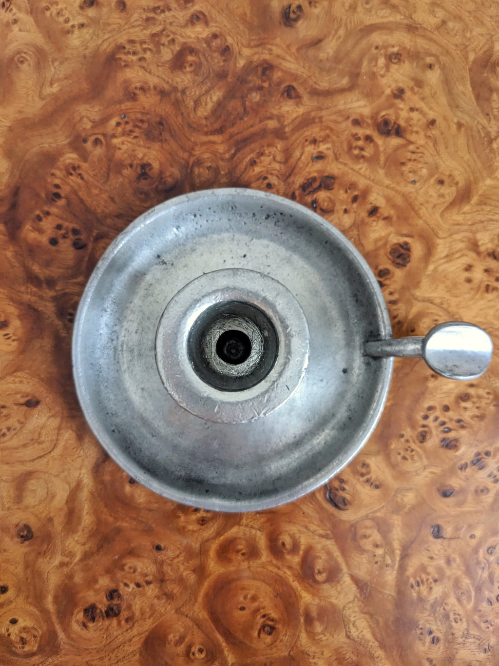 A birds eye view of a 'Wee Willy Winky' style vintage silver candle holder on a wooden surface with a knotted wood grain pattern.