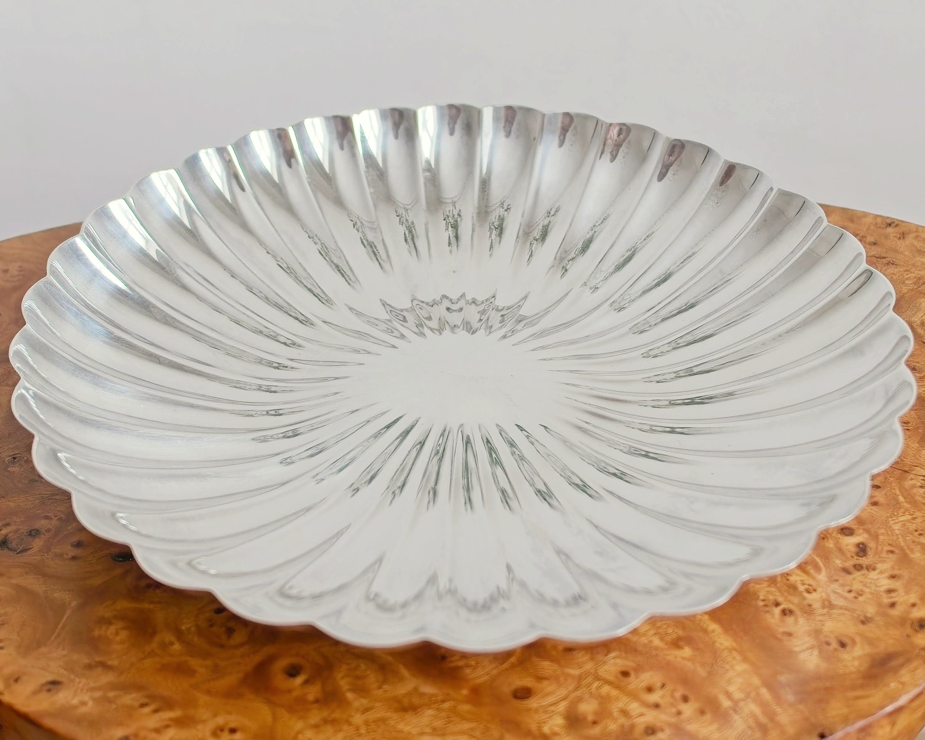 A close up of a vintage scalloped silver decorative bowl on an antique Georgian burr wood table.