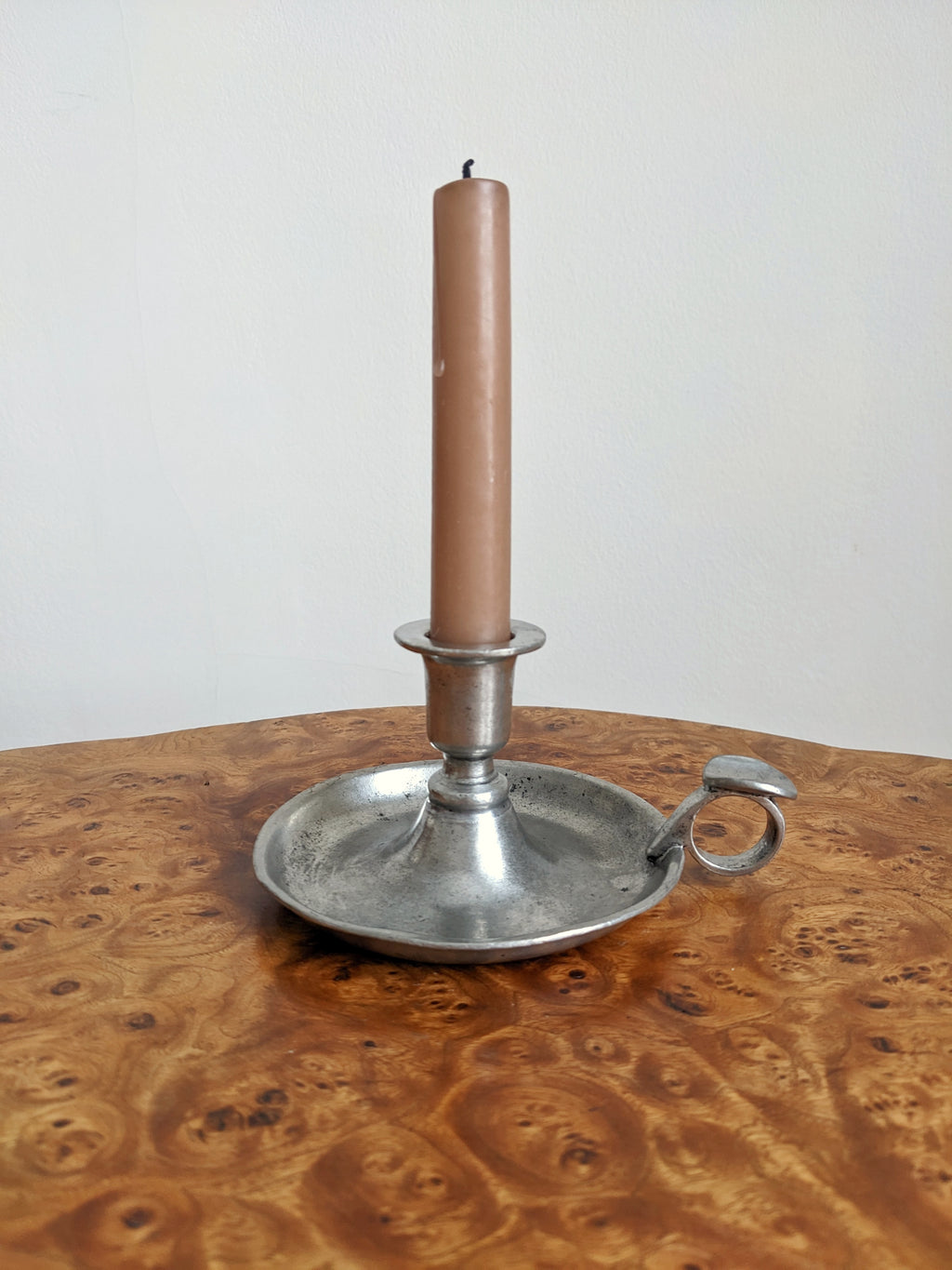 A Georgian style silver candle holder with a pink candle on a burr walnut side table.