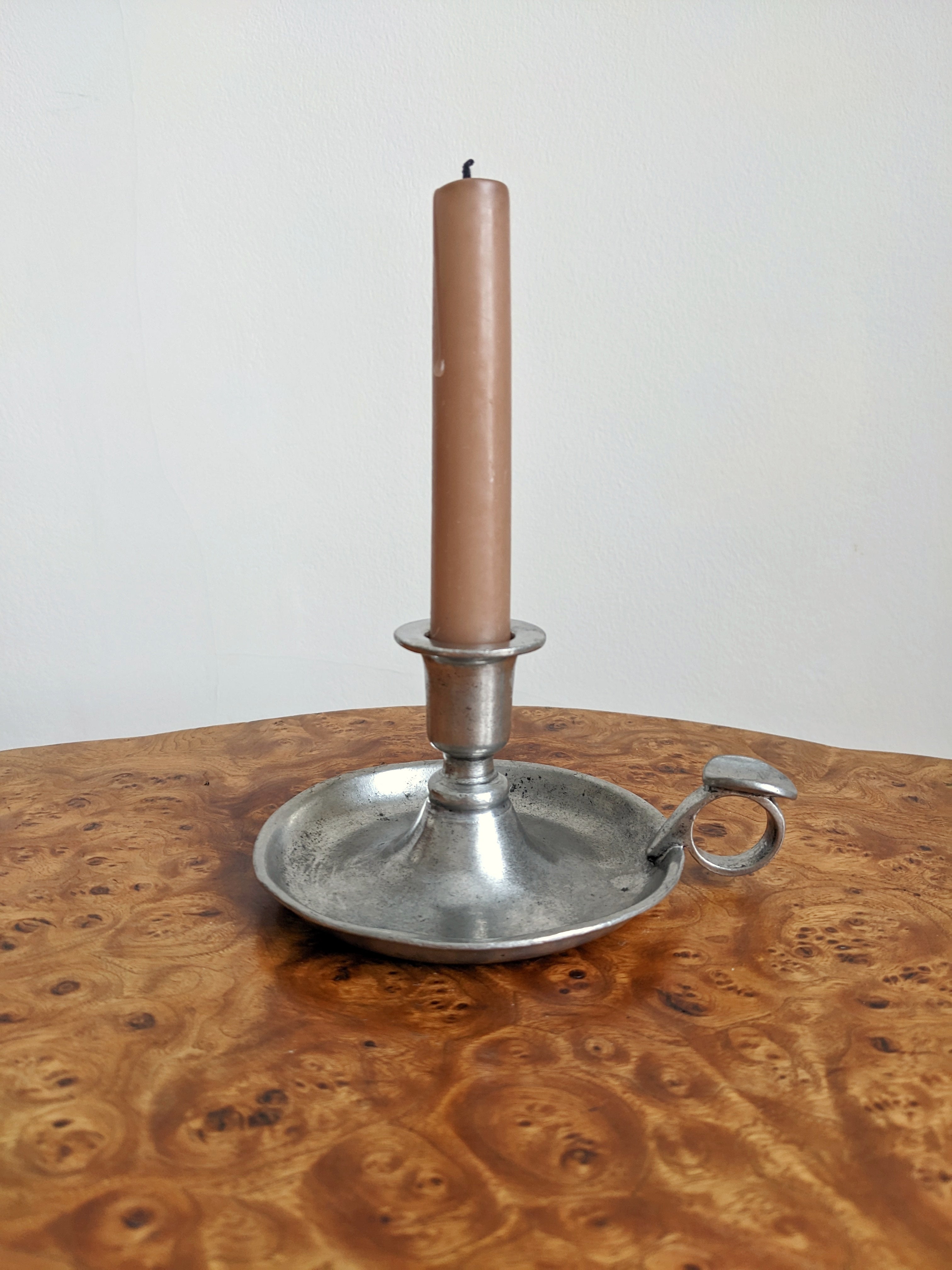 A Georgian style silver candle holder with a pink candle on a burr walnut side table.