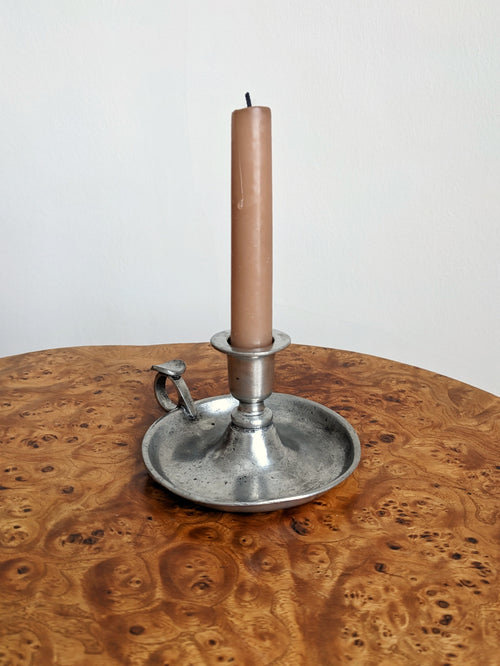 A pink candle in an antique style vintage metal candlestick holder on a wooden surface with a white background.