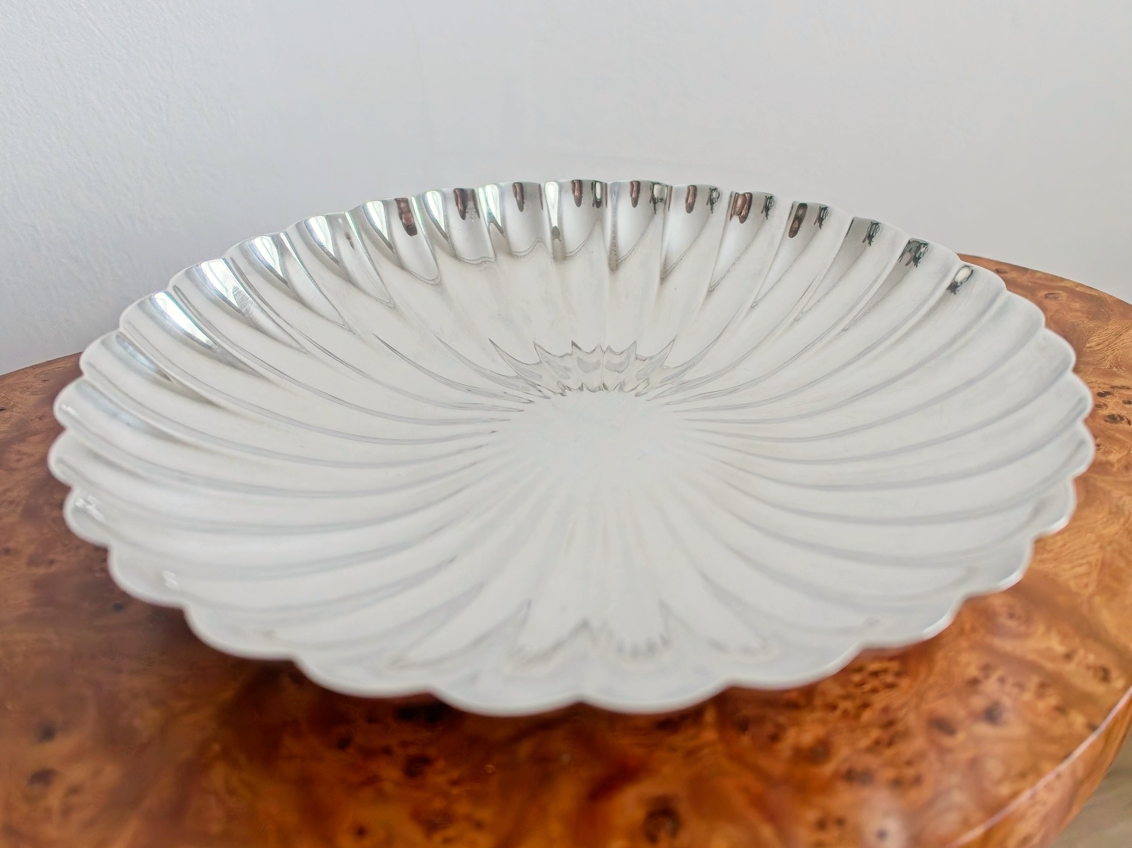 A close up of a vintage scalloped silver decorative bowl on an antique Georgian burr wood table.